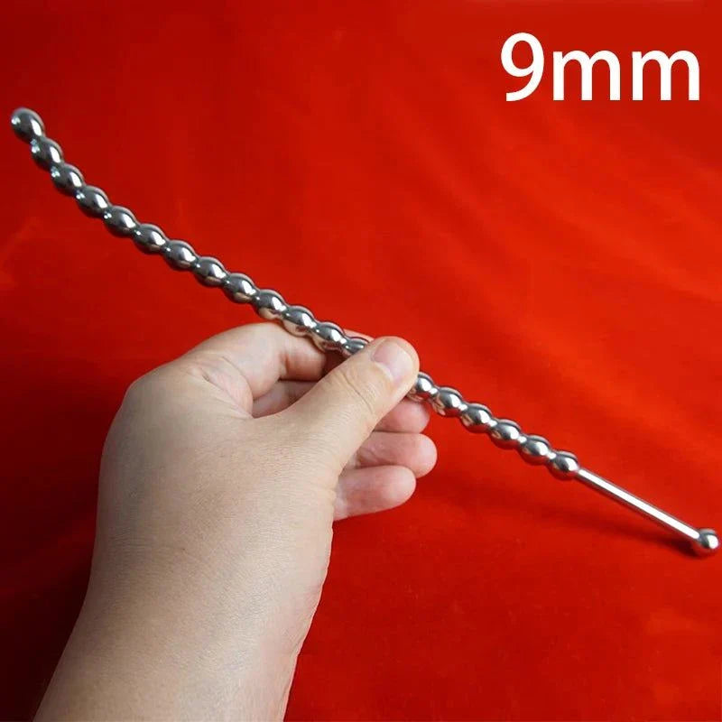 Curved stainless steel urethral insert penis plug with beaded shaft held in hand on red background