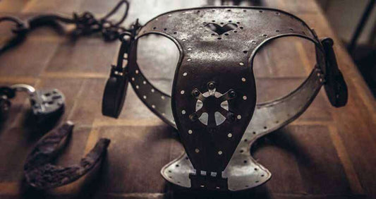 Antique iron chastity belt with heart-shaped cutout on wooden table, symbolizing historical chastity and My Dark Passion collection