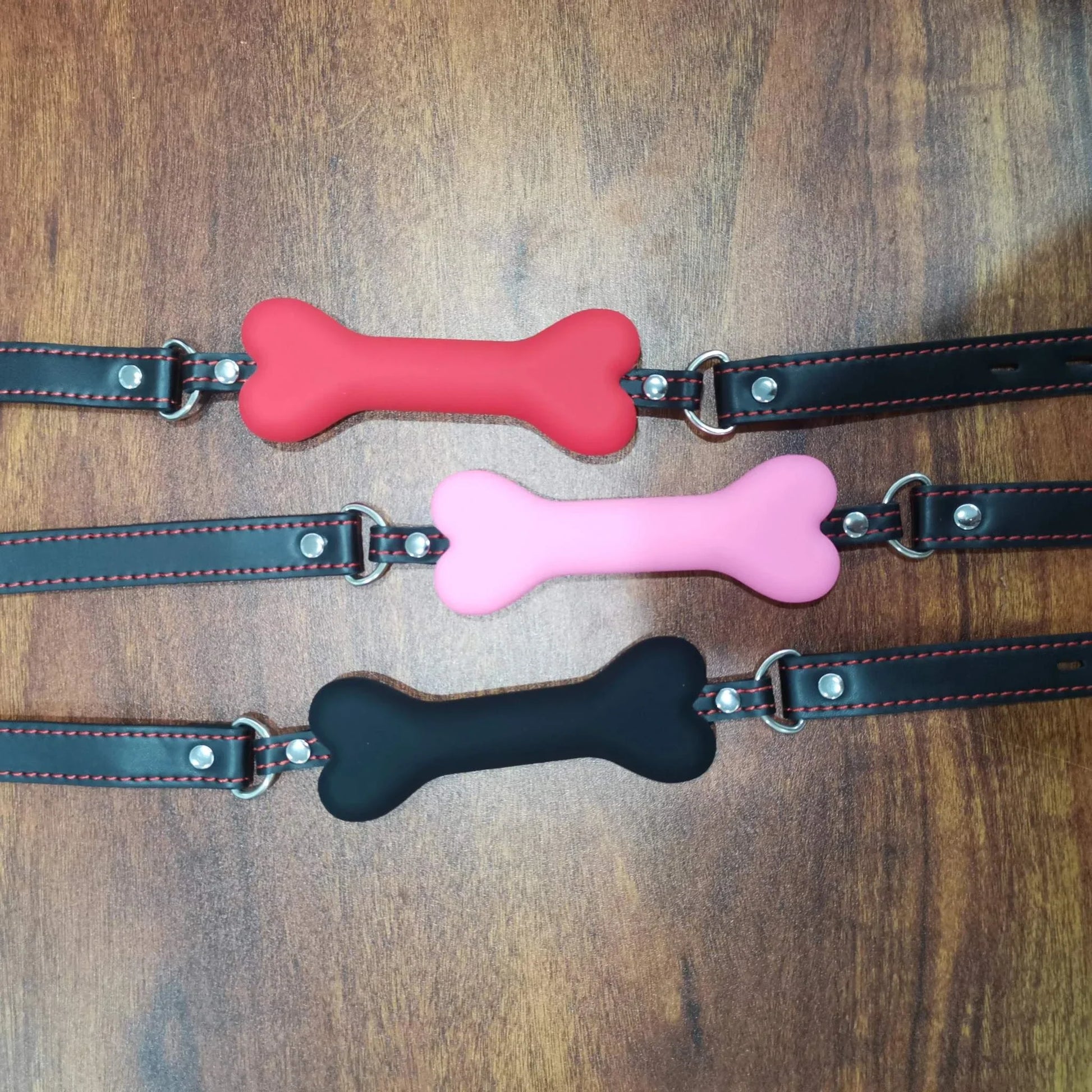 Soft harness mouth silicone dog-bone ball gags in red, pink, and black with adjustable straps on wooden surface