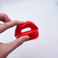 hand holding red soft silicone dog-bone style mouth gag for bondage play with adjustable harness straps