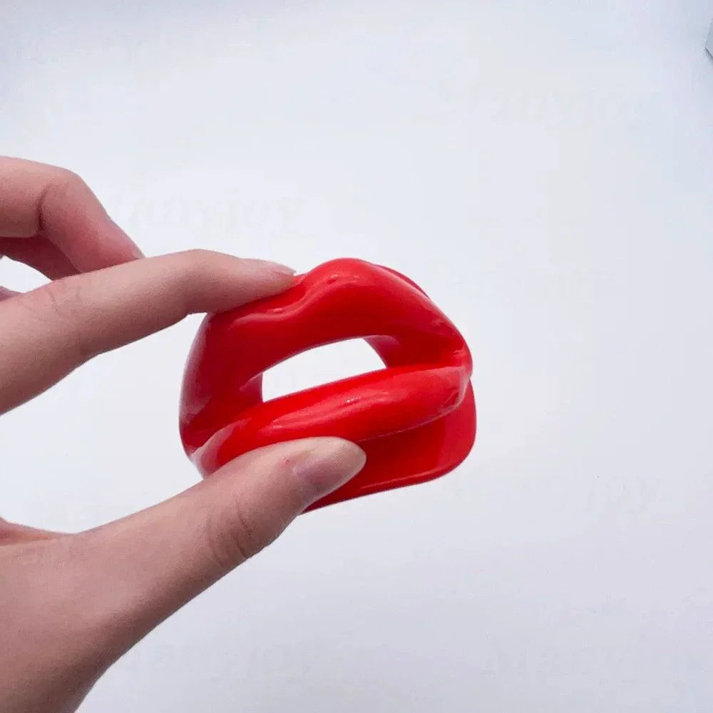 hand holding red soft silicone dog-bone style mouth gag for bondage play with adjustable harness straps